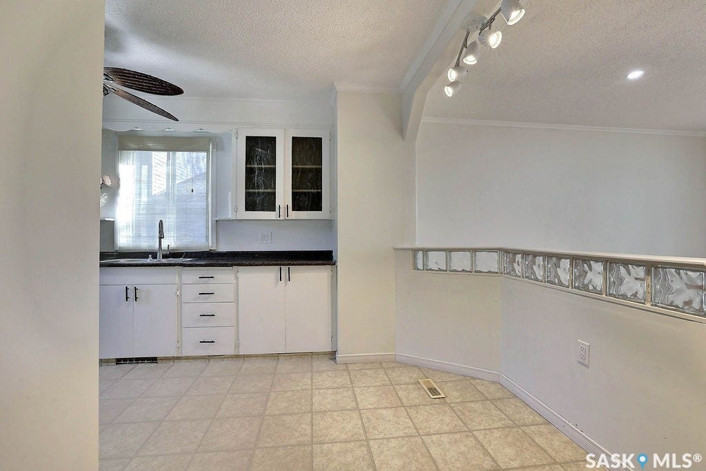 Kitchen area with white cabinetry, dark countertops, and a stainless steel faucet