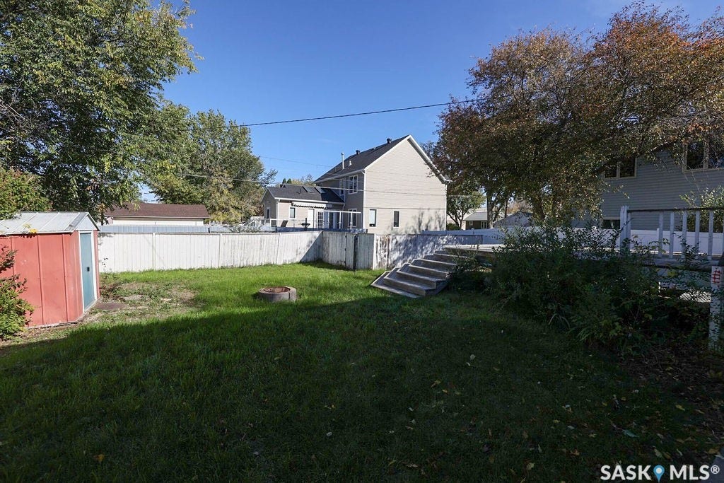Expansive backyard featuring a manicured lawn, a detached storage shed, a white privacy fence, and a concrete patio with steps