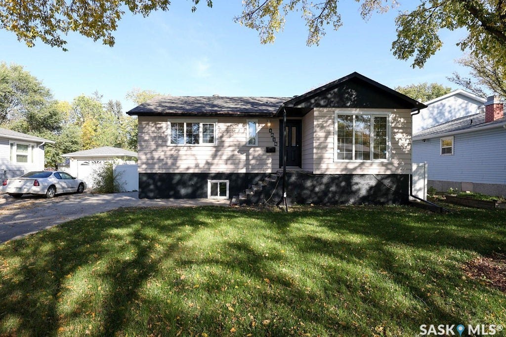 Split-level residence featuring light-toned siding, dark foundation, and a detached garage