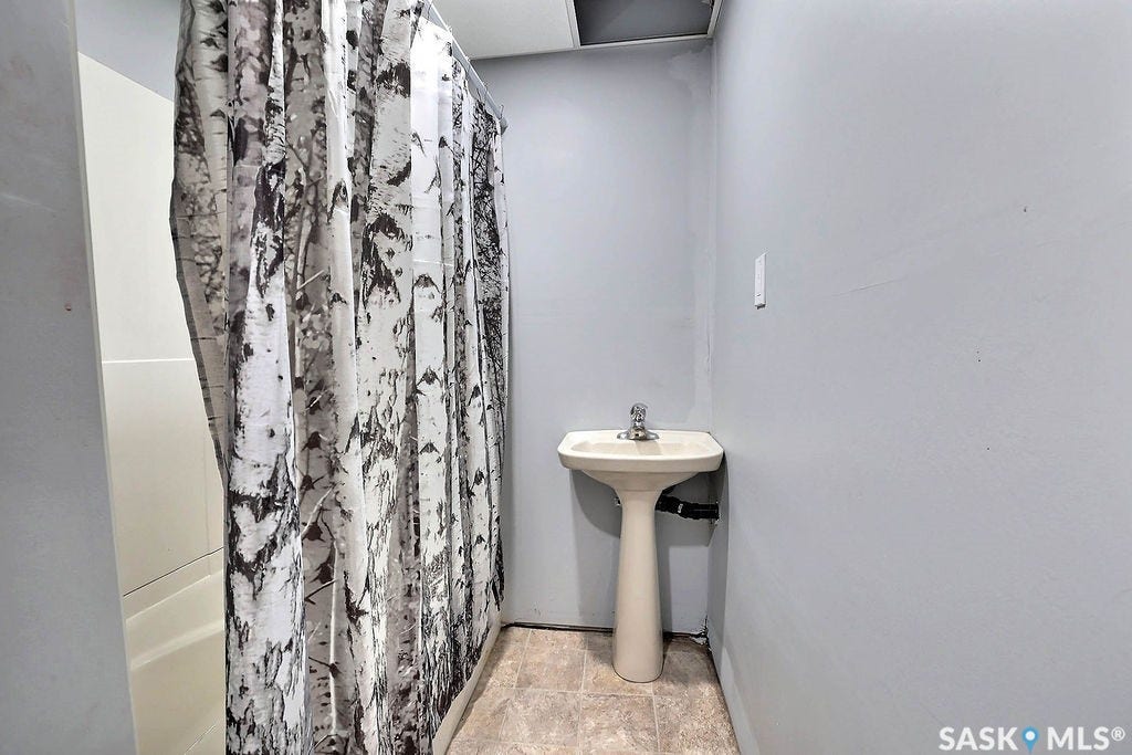 Pedestal sink with chrome faucet, tub/shower combination, and light gray wall paint