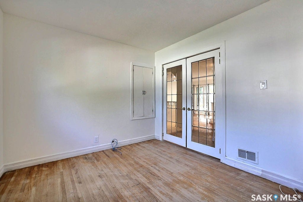 Spacious room featuring warm wood-finish flooring, white painted walls, and abundant natural light from dual glass doors with multiple panes