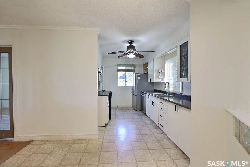 Kitchen featuring white cabinetry, dark countertops, a stainless steel sink with a gooseneck faucet, and ceiling fan