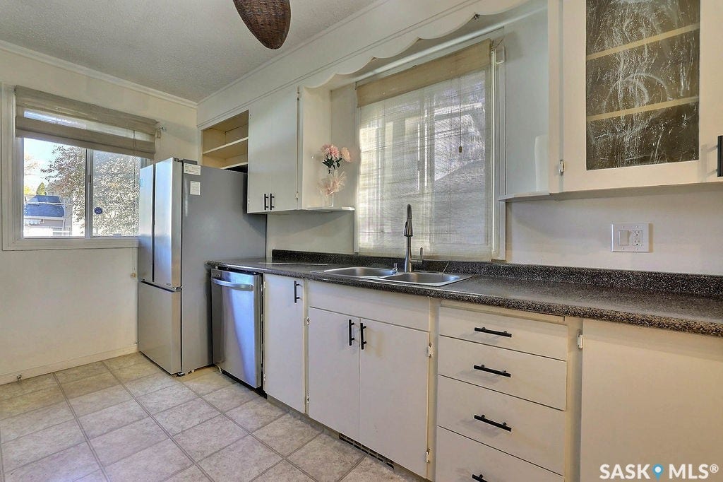 White cabinetry with black hardware, stainless steel appliances, dual basin sink with a high-arc faucet, speckled countertop, and tiled flooring