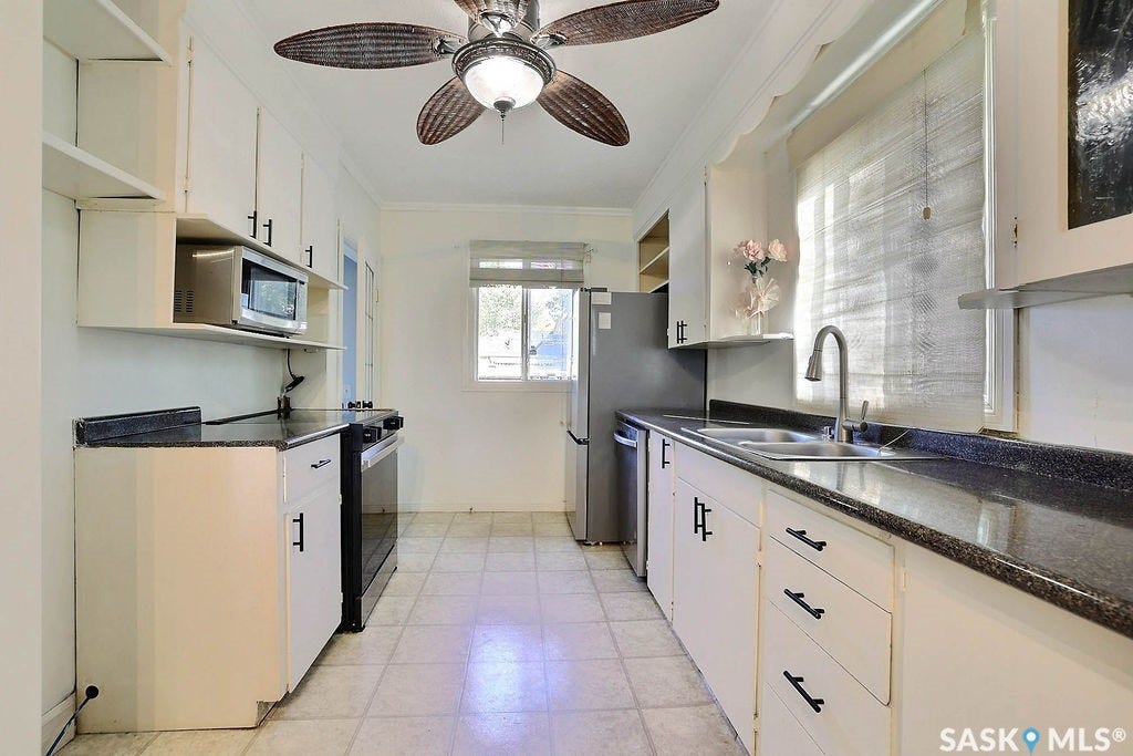 White cabinetry with black hardware, dark countertops, built-in microwave, stainless steel refrigerator, and dual basin sink