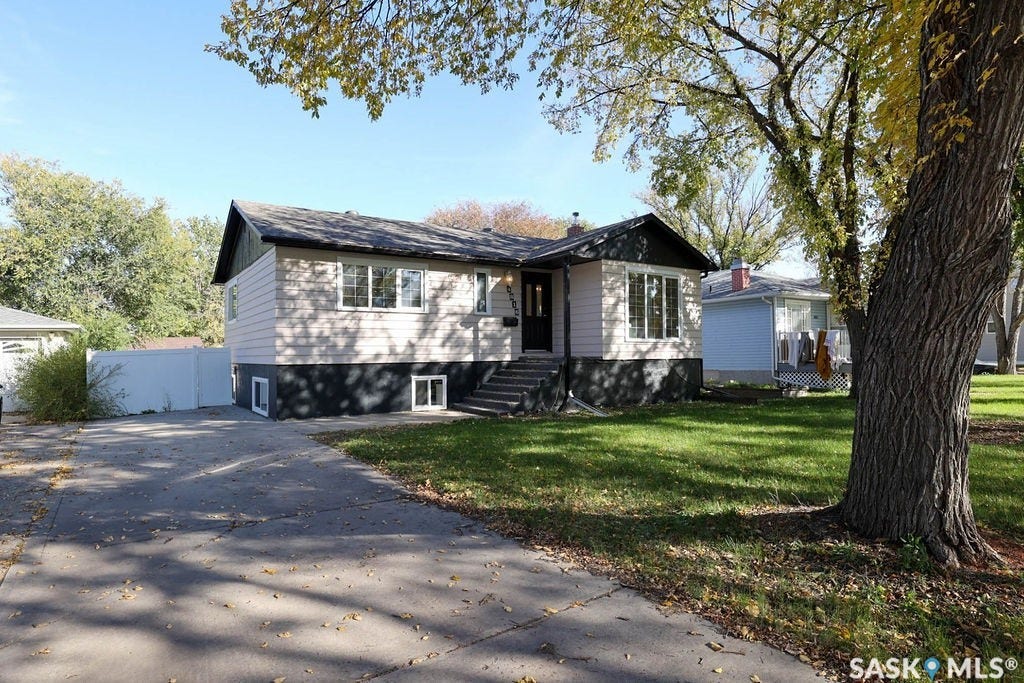 Single-story residence featuring light-colored siding, a dark roof, and a mature tree