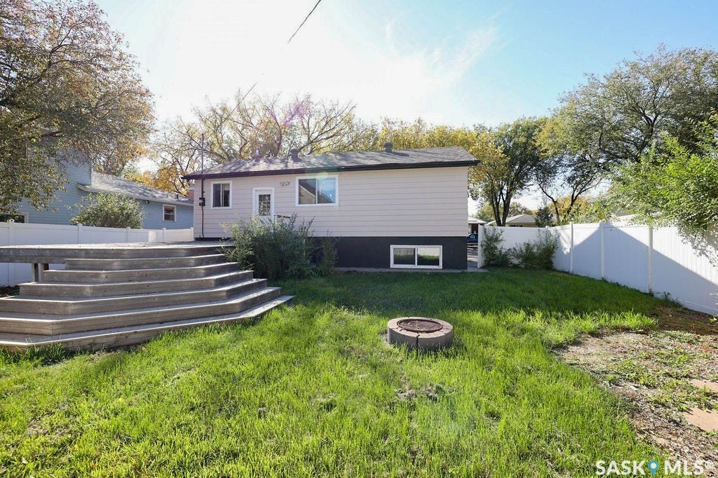 Spacious backyard with mature landscaping and established trees, featuring a curved composite deck with multiple levels, manicured lawn, and a fire pit