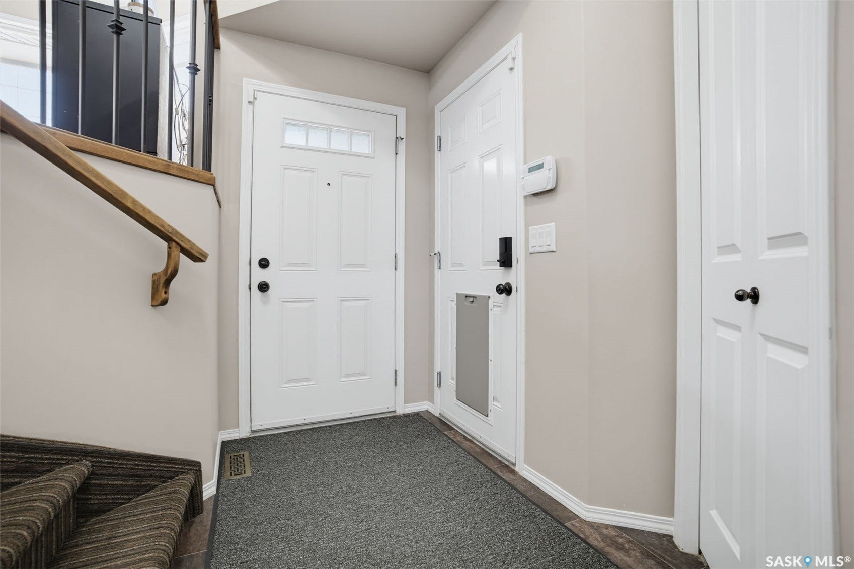 Entryway featuring a white paneled door with glass inserts, wood-finish flooring, and a carpeted staircase with a wood handrail