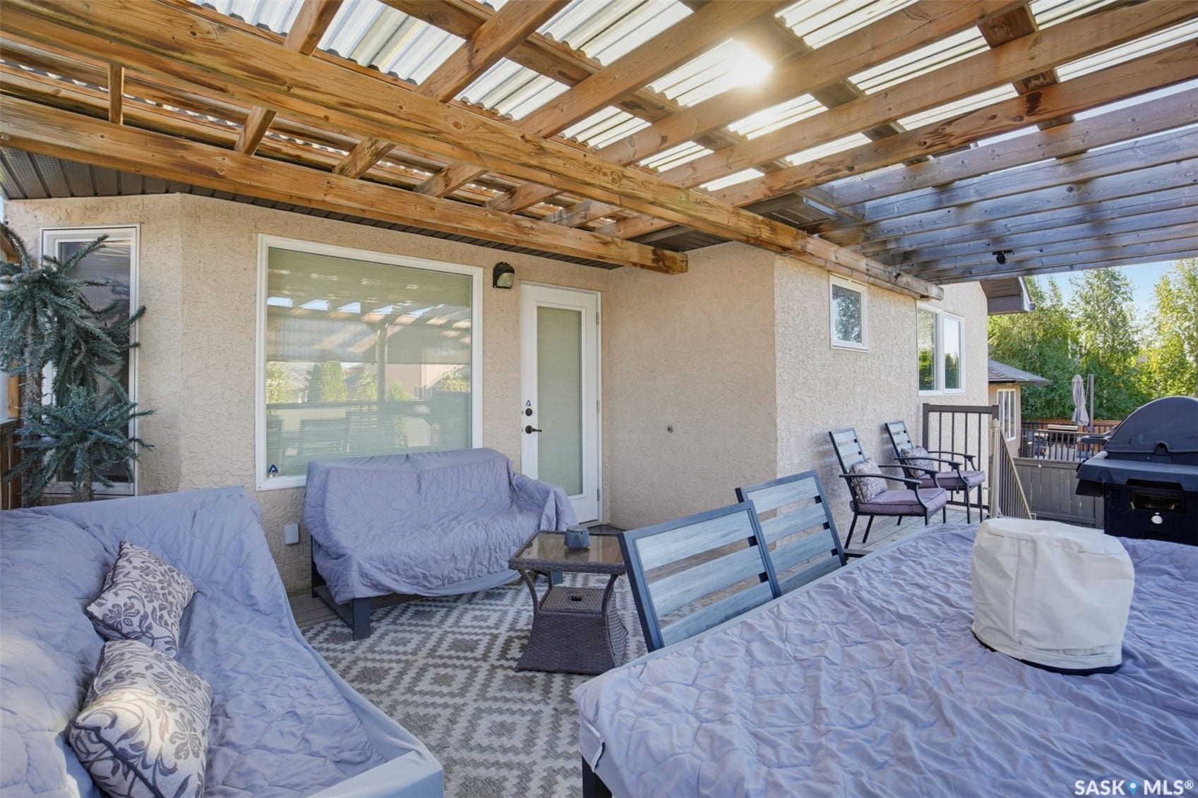 Expansive covered patio with exposed wooden beam structure and integrated skylights, featuring built-in seating areas, a gas grill, and direct access to the home's sliding glass doors