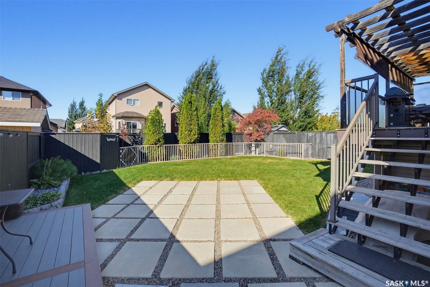 Expansive backyard featuring a manicured lawn, a large paver patio, a multi-level wood deck, and a wooden pergola structure