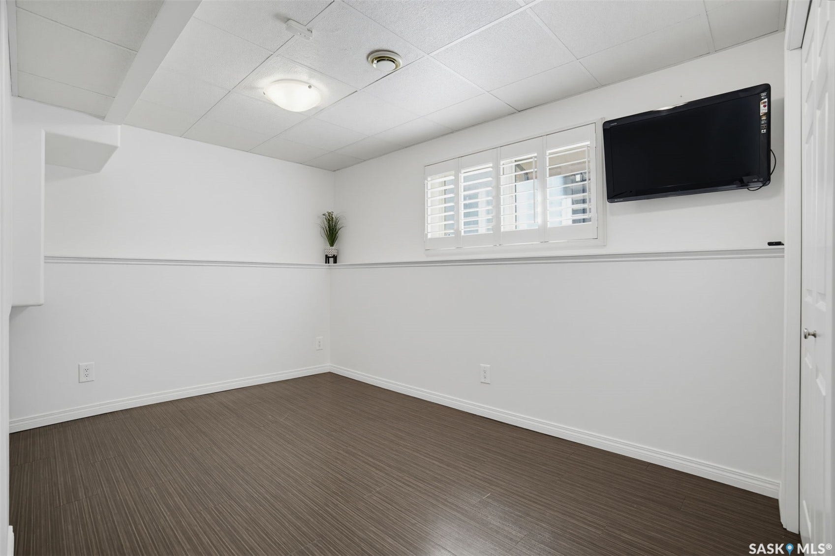 Bright, versatile interior space featuring crisp white walls with horizontal shiplap detailing, dark wood-finish flooring, recessed ceiling lighting, and a wall-mounted flat-screen television