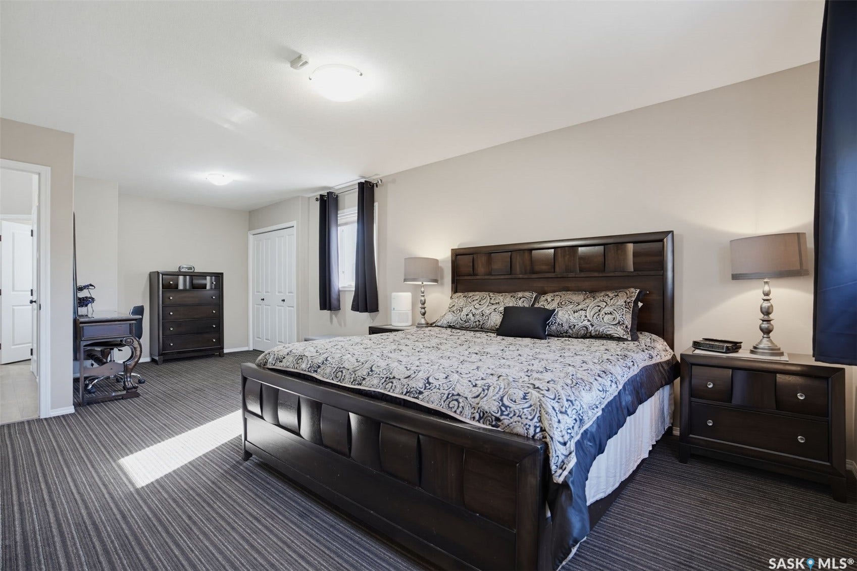 Spacious room featuring neutral wall tones, striped carpeting, a window with dark drapery, and a white bi-fold closet door