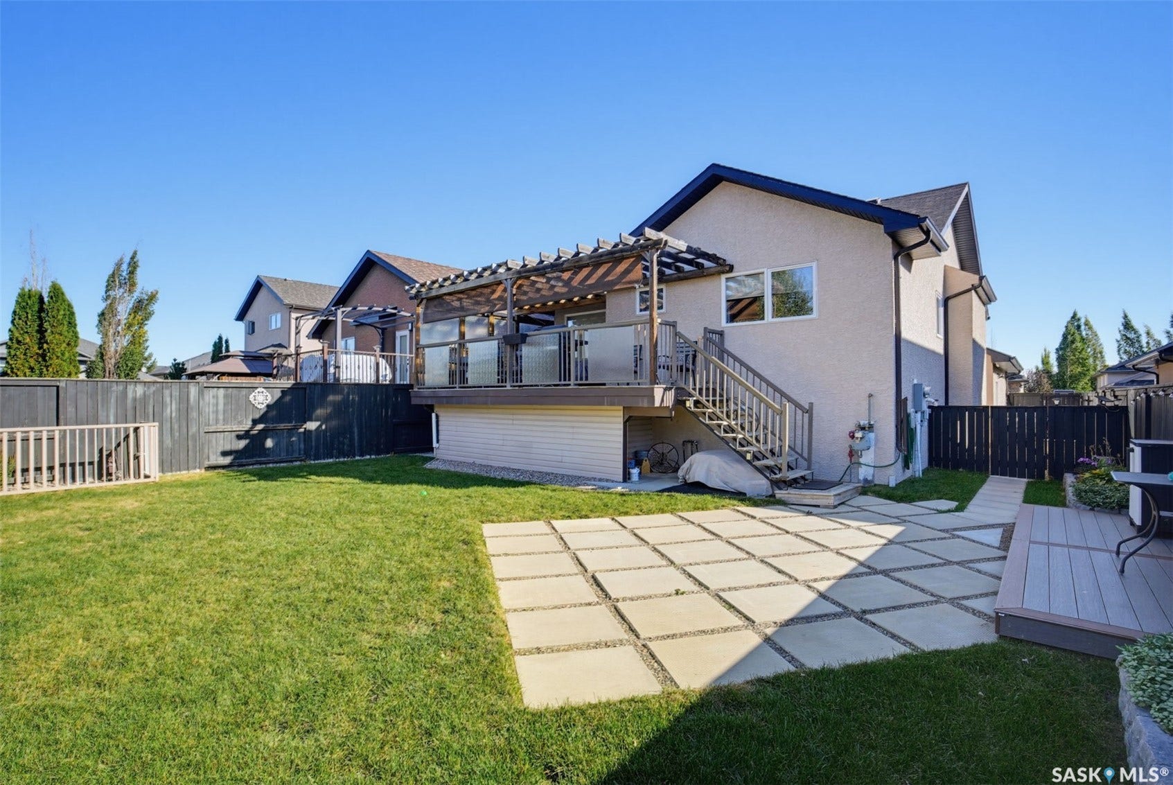 Expansive backyard featuring a manicured lawn, multi-level deck with glass railing, and a pergola