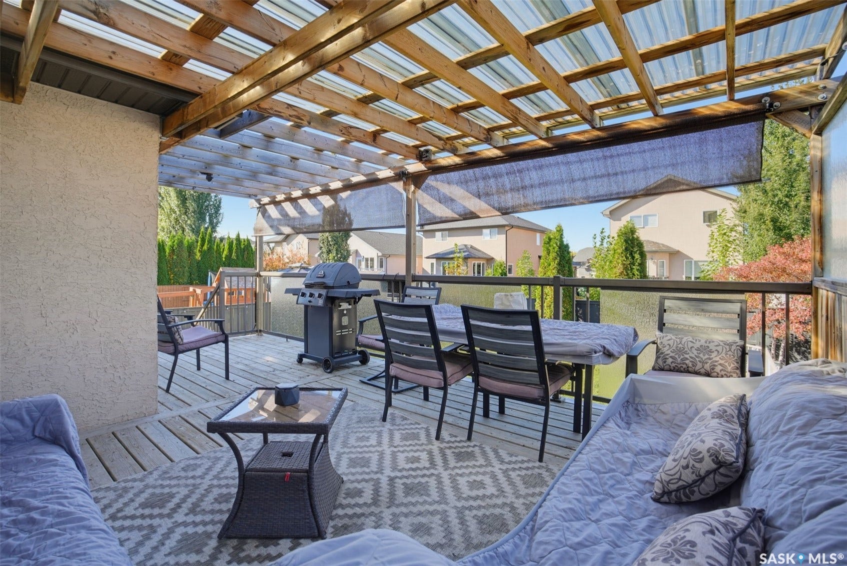 Expansive deck featuring a wood pergola with clear roofing, glass panel railing, and outdoor roller shades