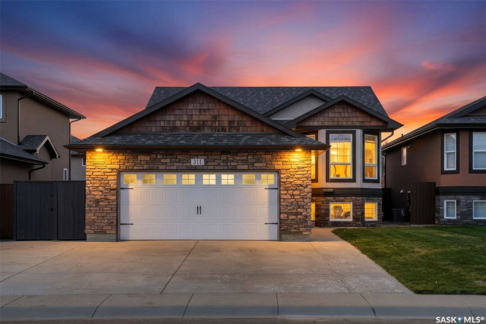 Architectural home with a stone and wood shingle exterior, featuring a two-car garage, concrete driveway, and established front yard landscaping