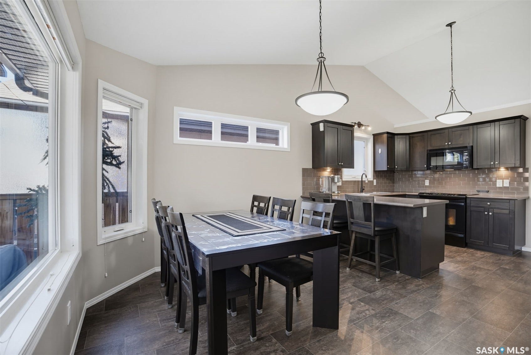 Kitchen and dining area featuring dark wood-finish cabinetry, tile flooring, vaulted ceilings, and pendant lighting