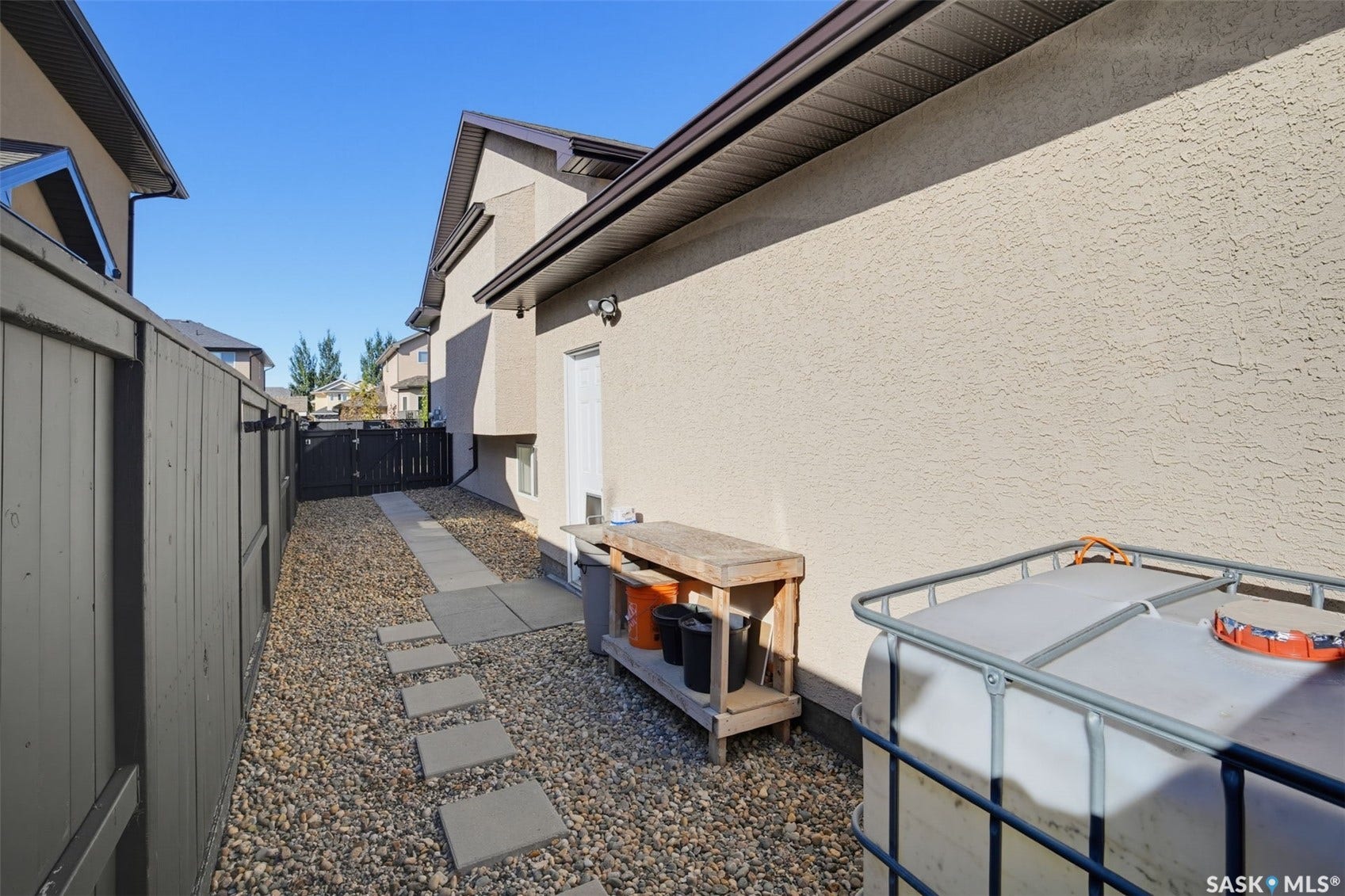 Gravel pathway with stepping stones, bordered by a privacy fence and stucco exterior