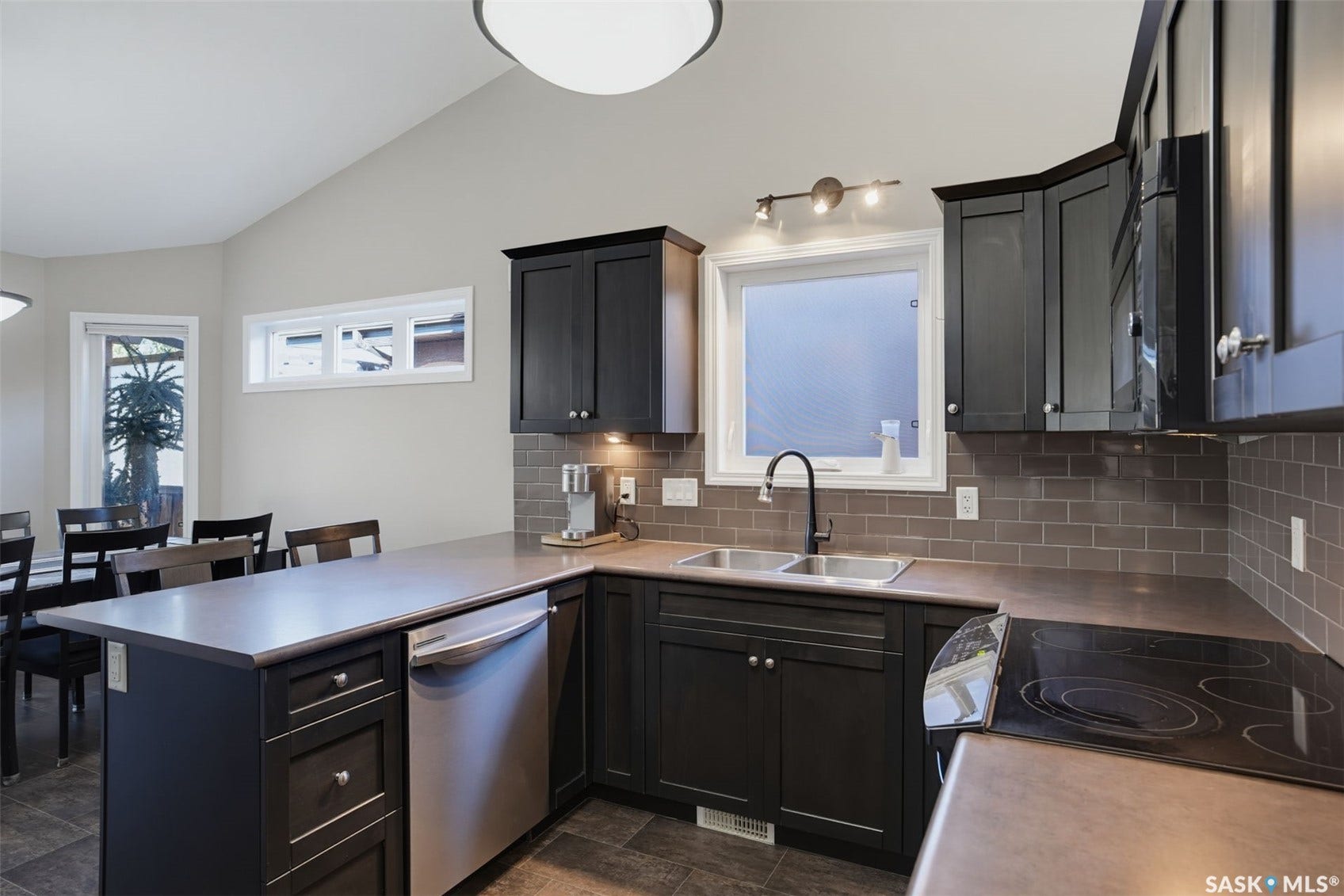 Kitchen featuring dark wood-finish cabinetry, stainless steel appliances, a double basin sink, and subway tile backsplash