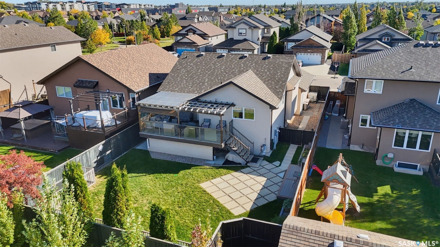 Spacious backyard featuring a manicured lawn, an expansive raised deck with glass railings, and an integrated pergola