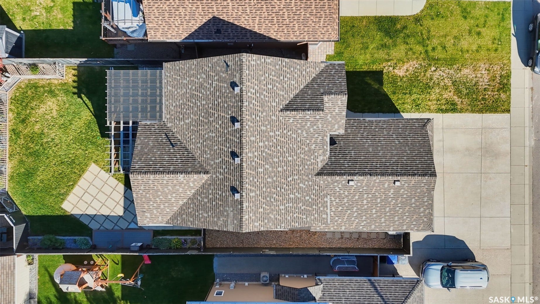 Multi-pitch shingle roof, paved driveway, concrete sidewalks, and a patio with a pergola structure