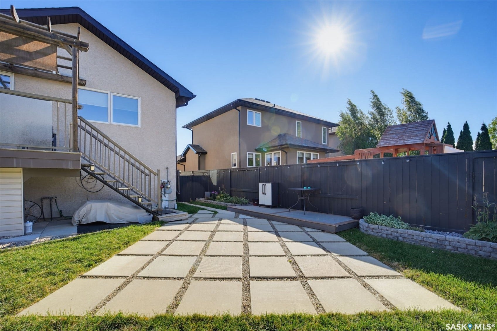 Expansive backyard featuring a large patio with concrete paver accents, a multi-level deck, dark wood fencing, and a built-in garden bed with stone retaining wall