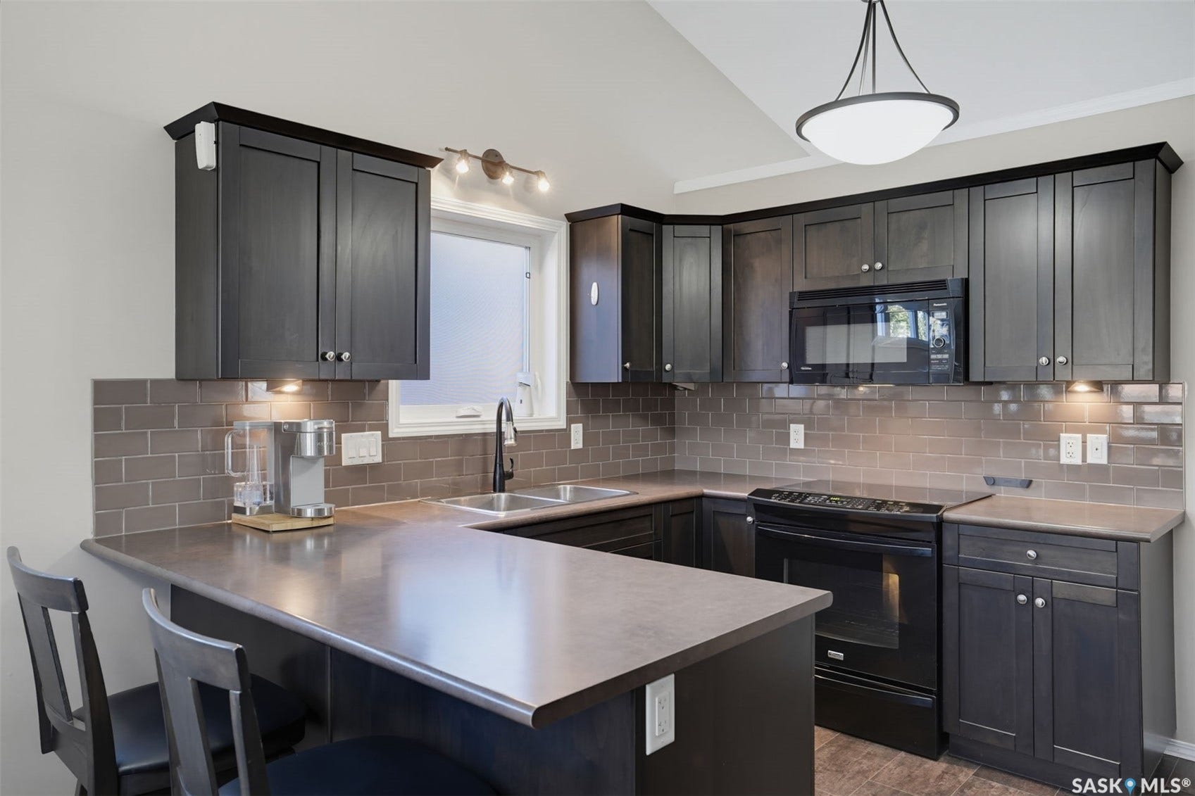 U-shaped kitchen featuring dark wood-finish cabinetry, subway tile backsplash, and a built-in microwave