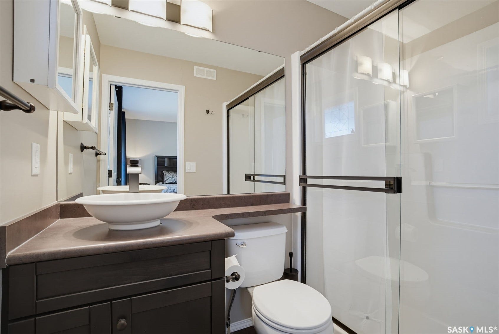 Modern bathroom featuring a dark wood-finish vanity with a contemporary vessel sink, quartz countertop, and matte black hardware