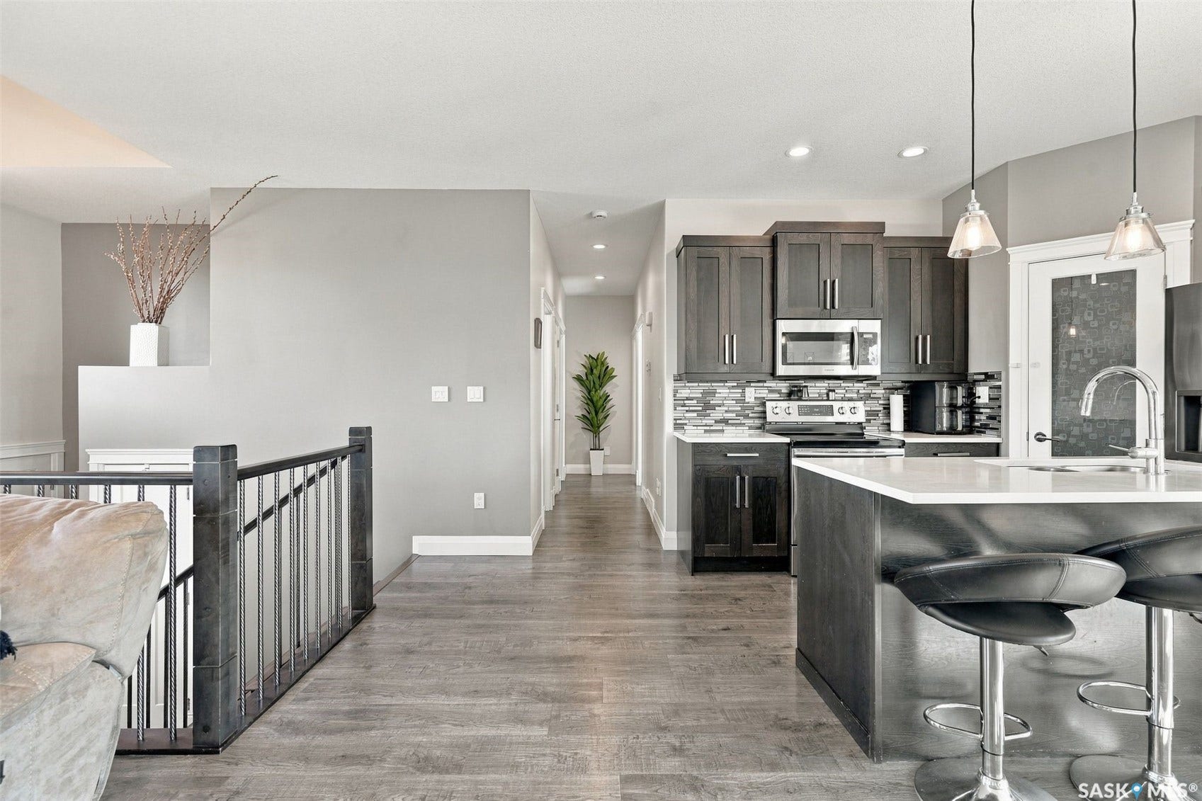 Modern kitchen featuring dark wood cabinetry, stainless steel appliances, a tile backsplash, and a large island with a white countertop