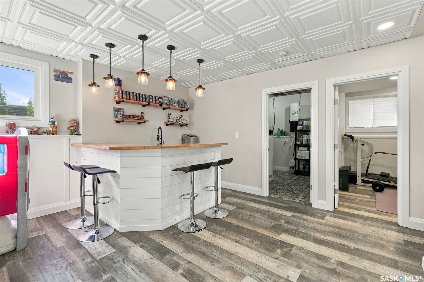 Wood-finish flooring, white shiplap bar with wood countertop, five pendant lights, and a decorative ceiling