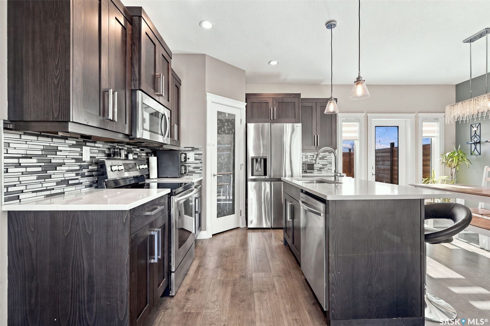 Kitchen featuring dark wood-finish cabinetry, stainless steel appliances, white countertops, a mosaic tile backsplash, and a central island with an integrated sink