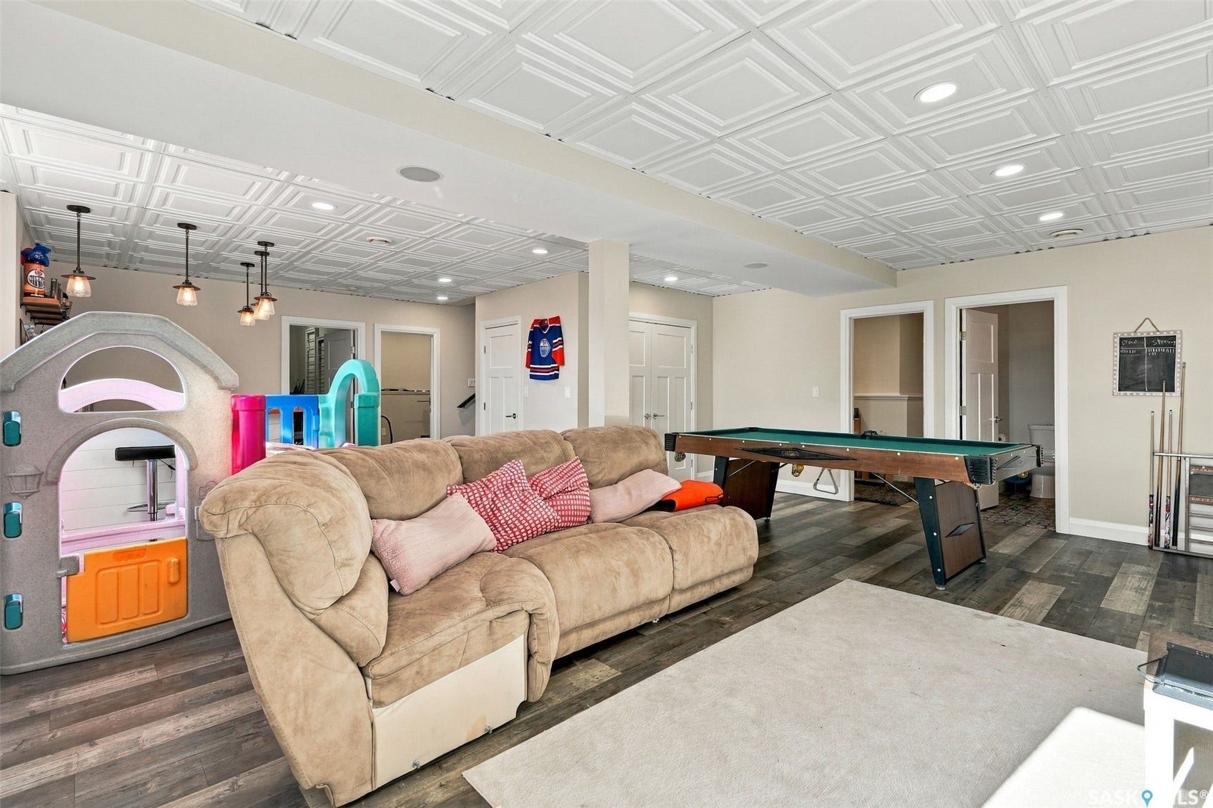 Recessed lighting, wood-finish flooring, and a decorative ceiling panel system are featured in this spacious recreation area