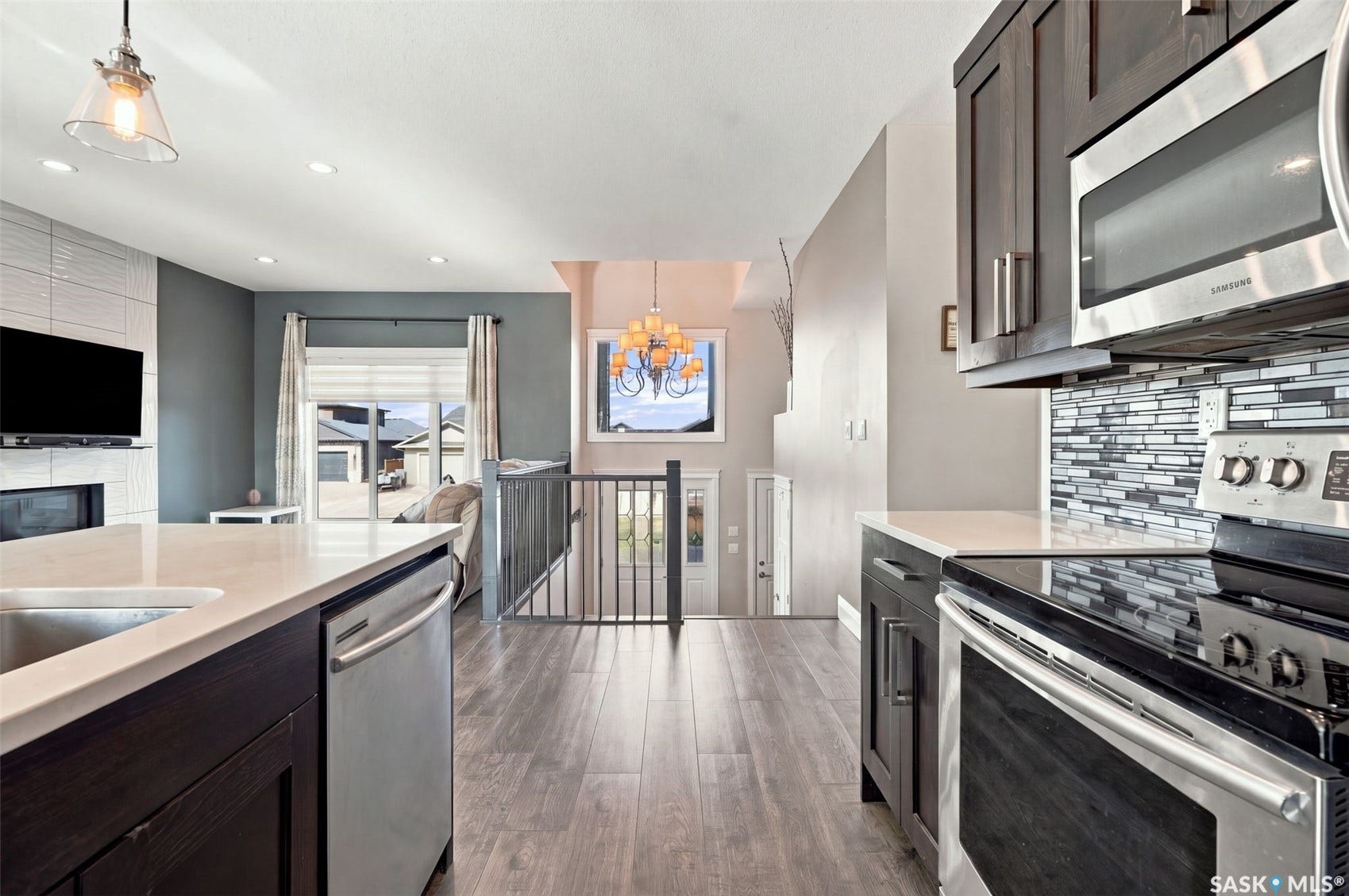 Wood-finish flooring, recessed lighting, and a kitchen featuring stainless steel appliances, dark cabinetry, and light-toned countertops