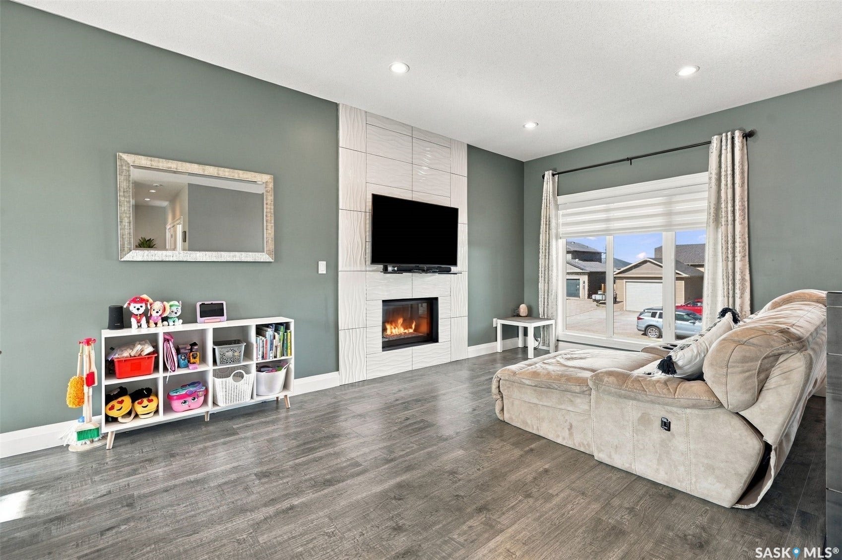 Wood-finish flooring, recessed lighting, and a linear fireplace with a textured tile surround