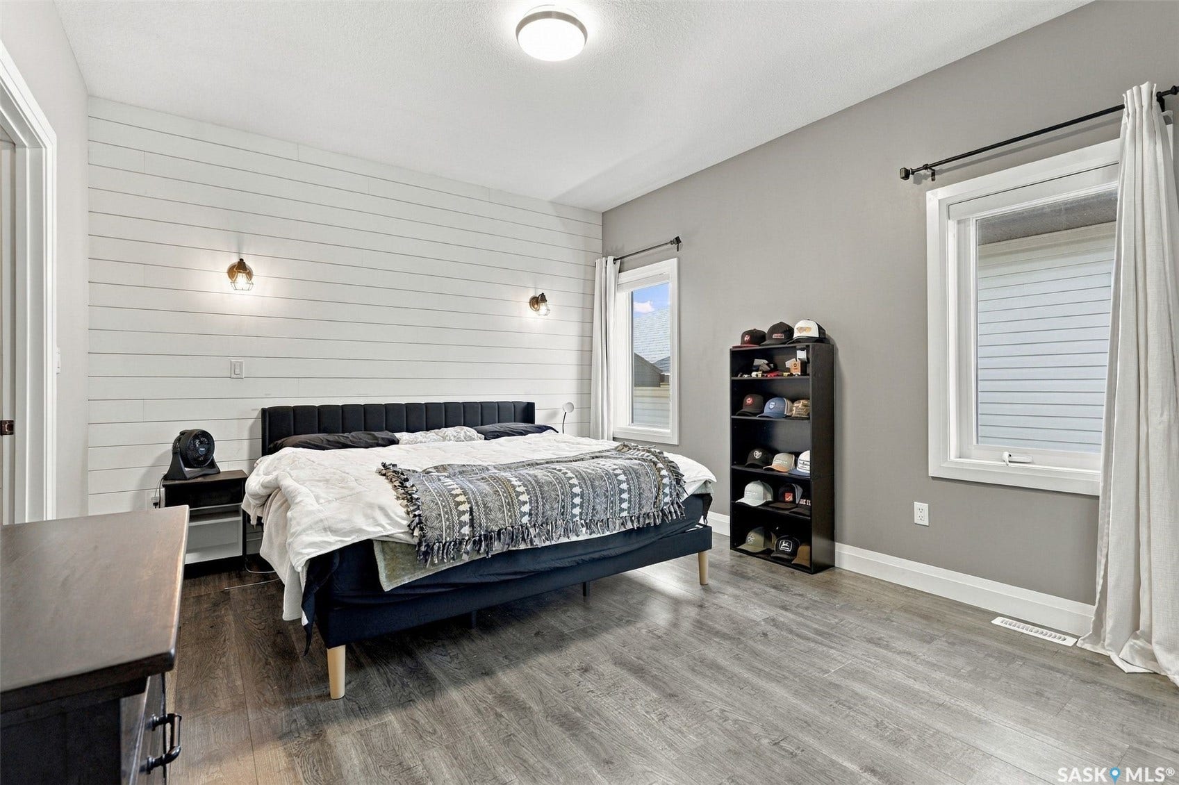 Wood-finish flooring, accent wall with horizontal paneling, two windows with white trim, recessed ceiling light, and two wall-mounted sconces