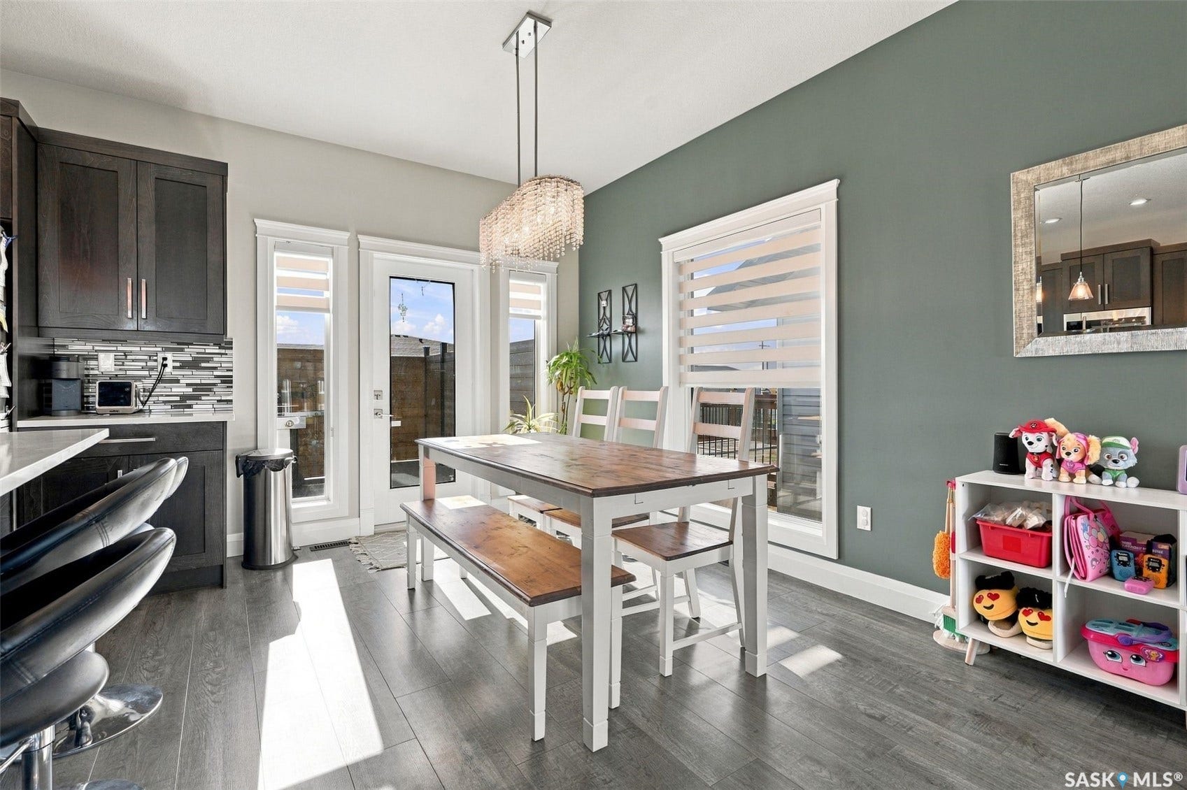 Wood-finish flooring, dark wood-finish cabinetry, mosaic tile backsplash, white trim, and a glass-paneled door