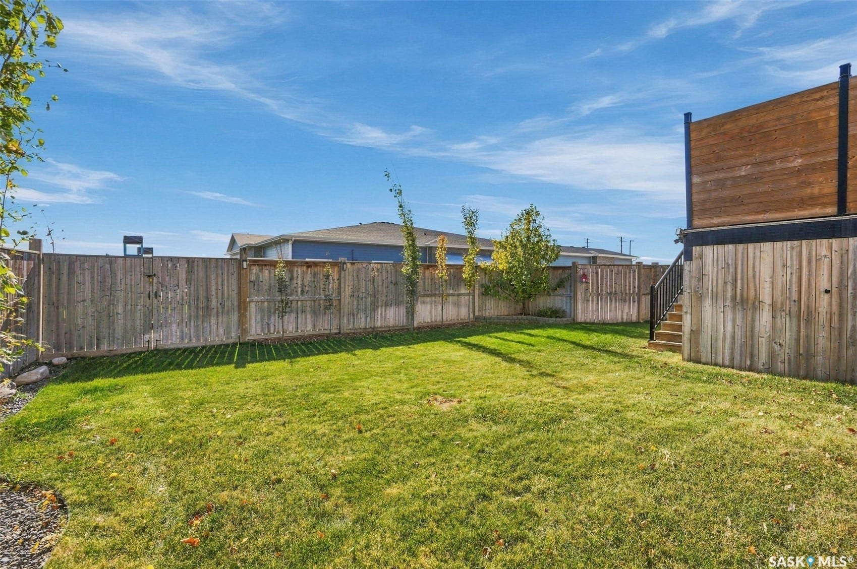 Expansive backyard featuring a manicured lawn, full privacy fencing, exterior stairs with metal railing, and a multi-level deck structure with wood siding
