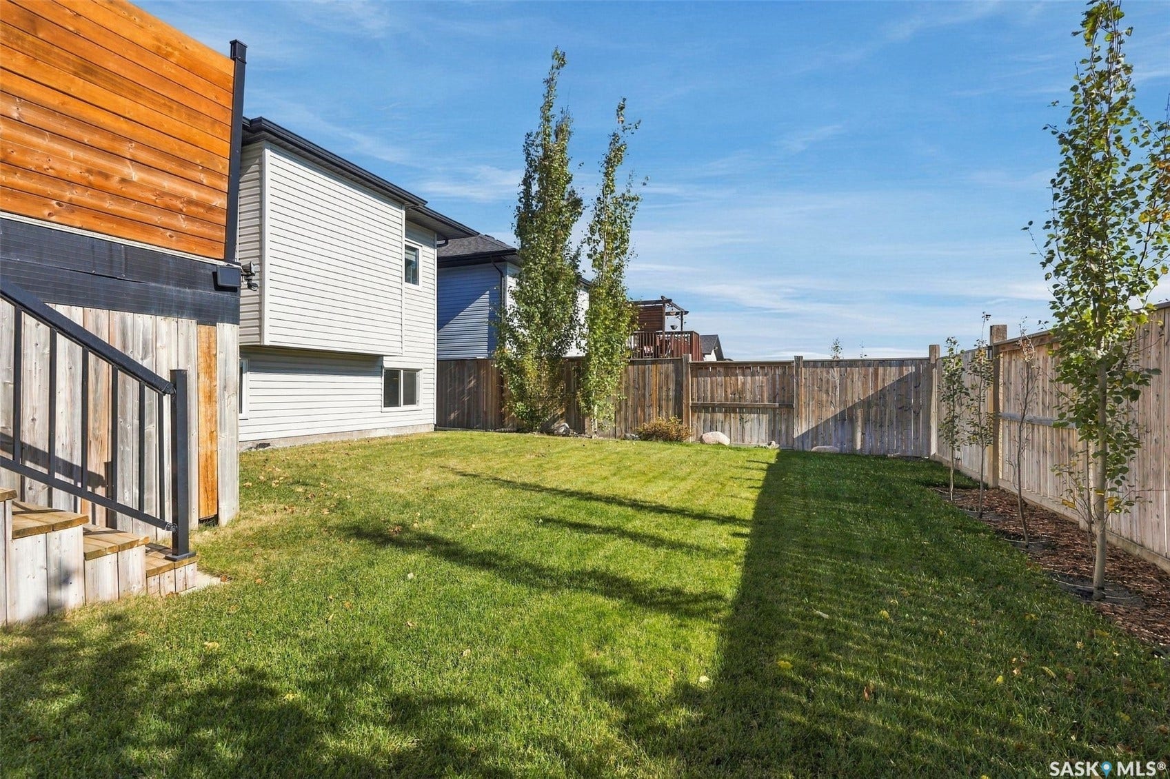 Expansive backyard featuring a manicured lawn, wood fencing, and mature trees