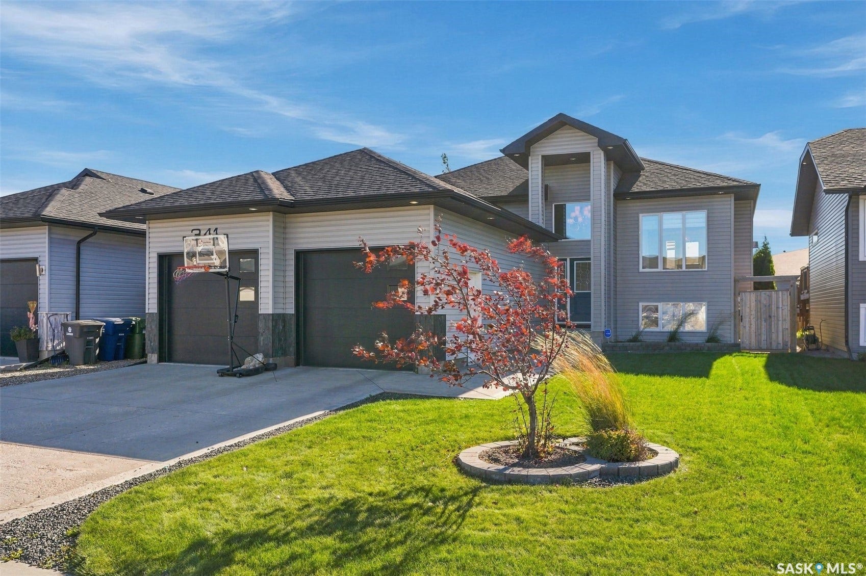 Contemporary exterior with partial stone detailing, an attached two-car garage, expansive concrete driveway, and a well-maintained front lawn with established landscaping