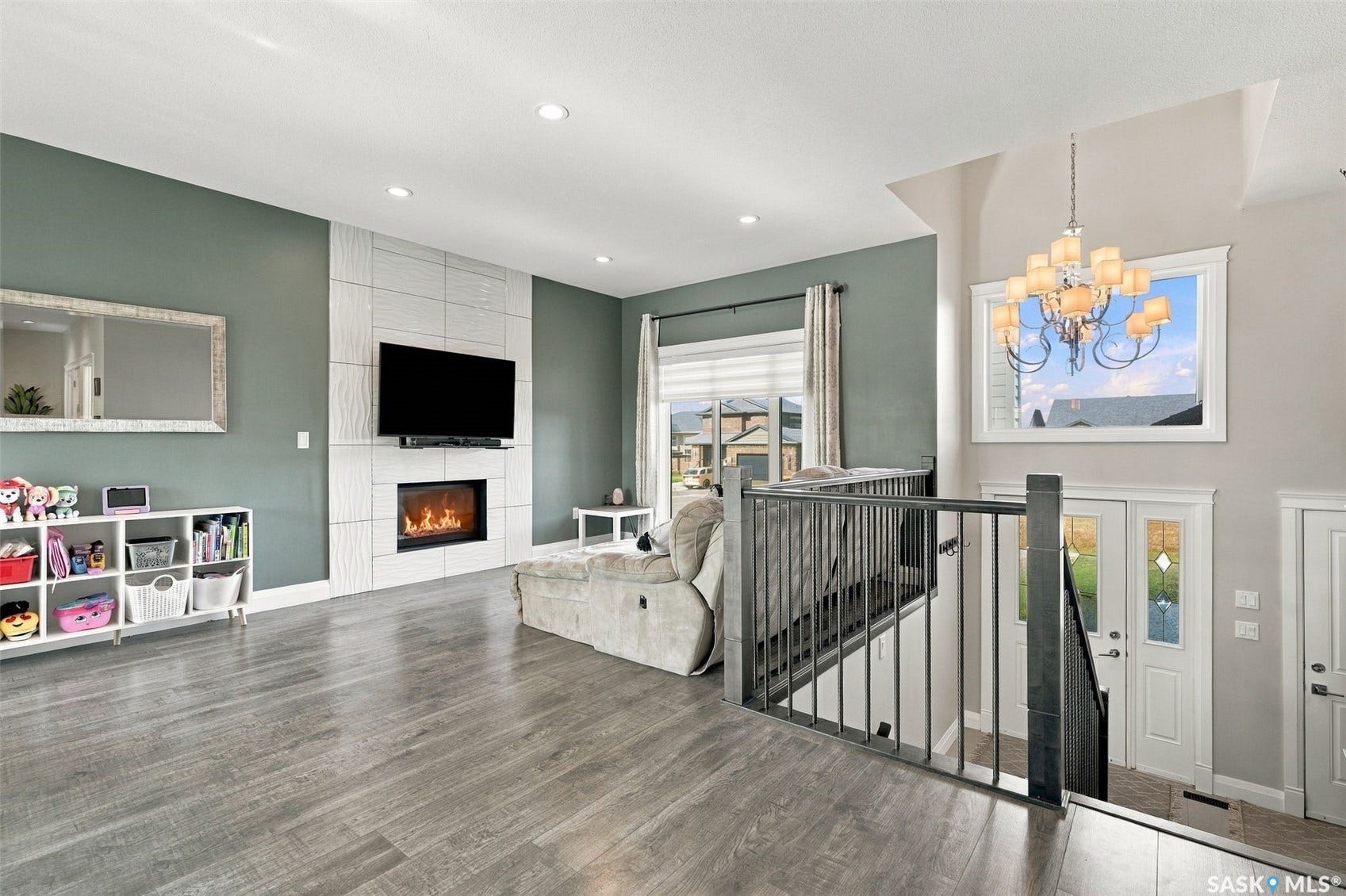 Tile-surround fireplace, recessed lighting, wood-finish flooring, staircase with metal railings, and a grand chandelier
