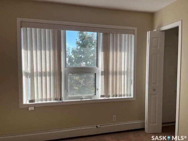 Large window with vertical blinds, baseboard heating unit, and wood-finish flooring