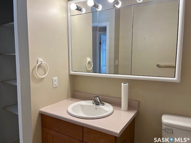 Vanity with an integrated sink, laminate countertop, wood-finish cabinetry, and overhead lighting