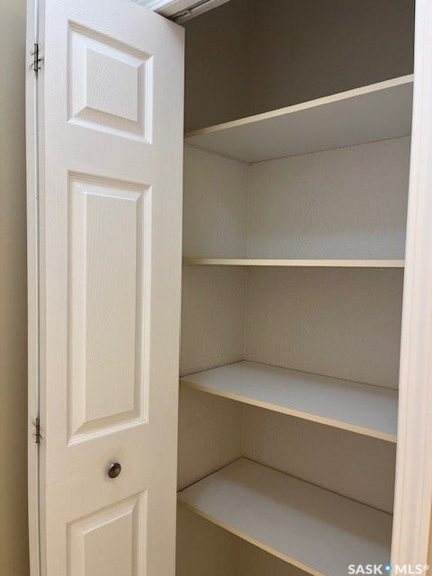 Interior storage closet with multiple fixed shelves, featuring a paneled bi-fold door with a round knob