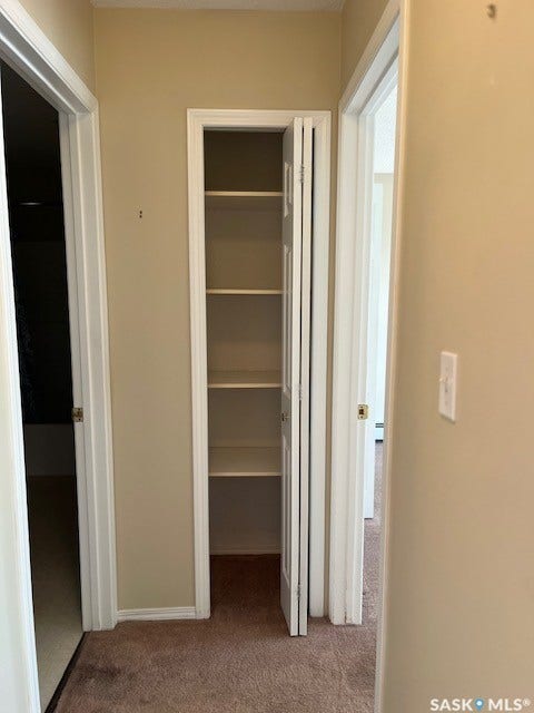 Hallway with neutral tone walls and brown carpet flooring