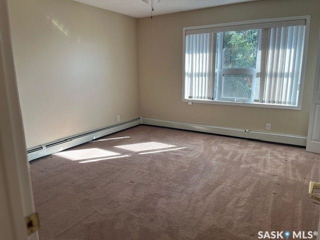 Bright, naturally lit living space featuring neutral wall finishes, carpet flooring, and expansive sliding glass doors with vertical blinds that flood the room with daylight