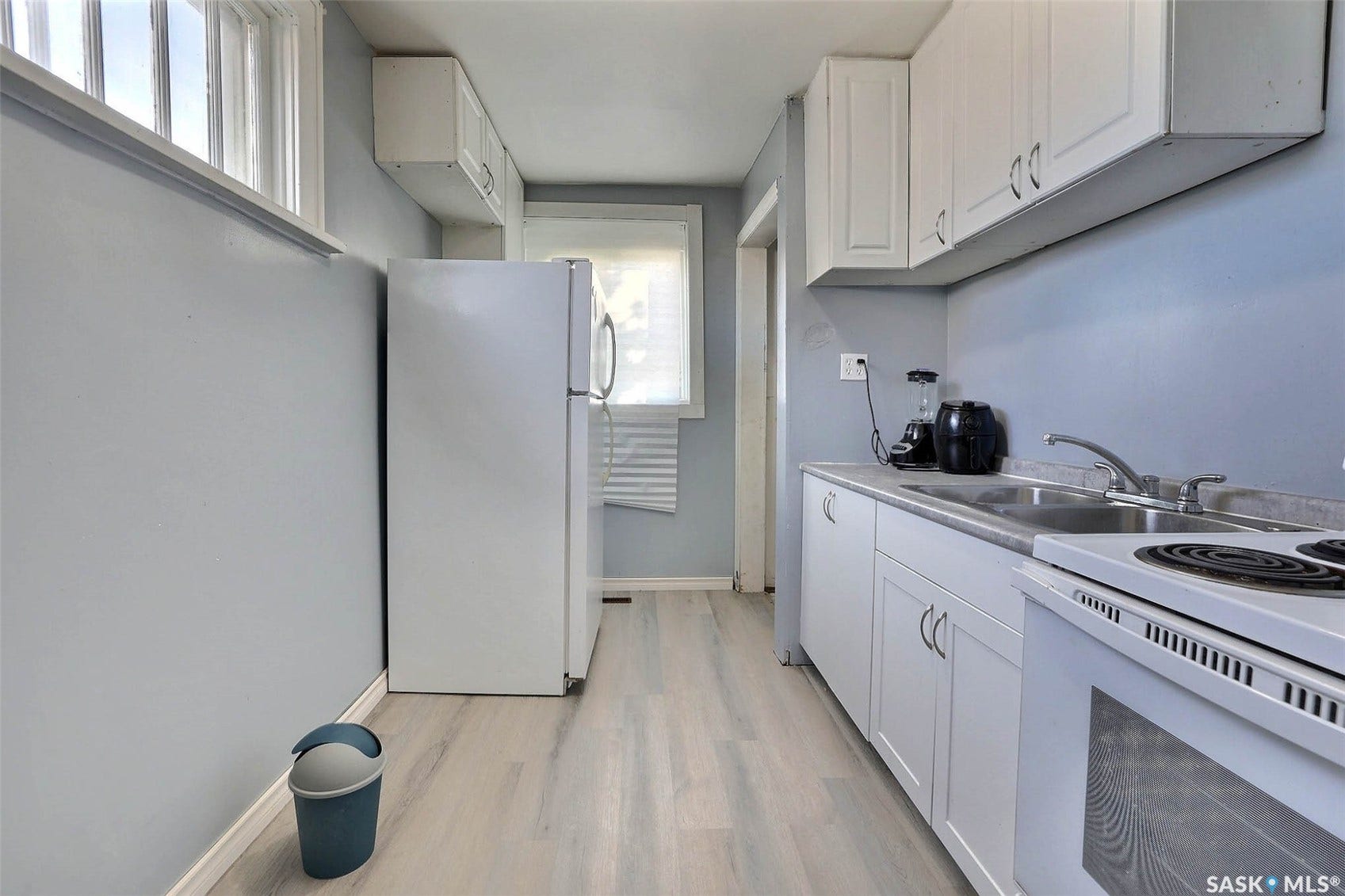 Contemporary kitchen with white cabinetry, light wood-finish flooring, a stainless steel sink, and white appliances