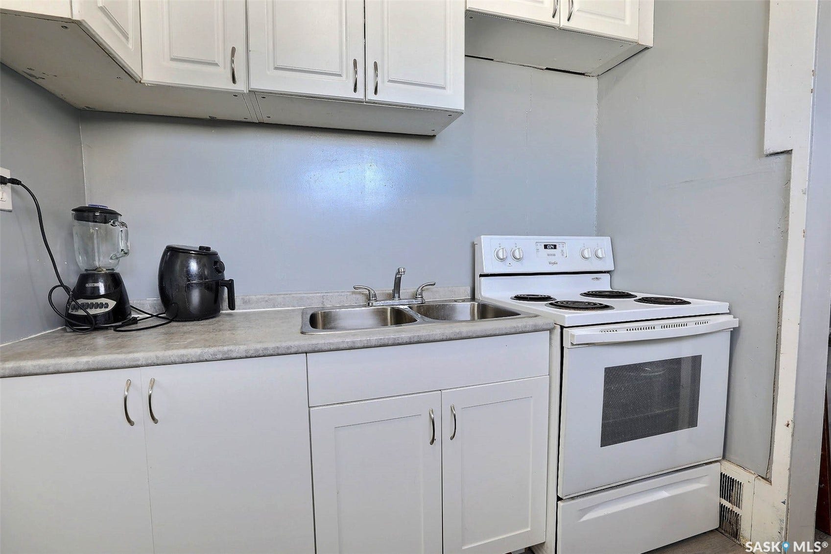 White cabinetry with silver hardware, dual basin stainless steel sink, countertop space, and white range