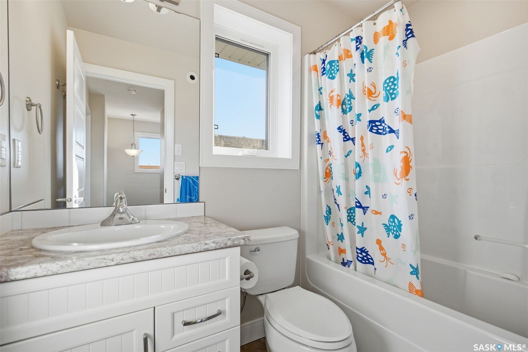 Bathroom featuring a white vanity with paneling, a countertop with a light speckled finish, a built-in bathtub, and a window