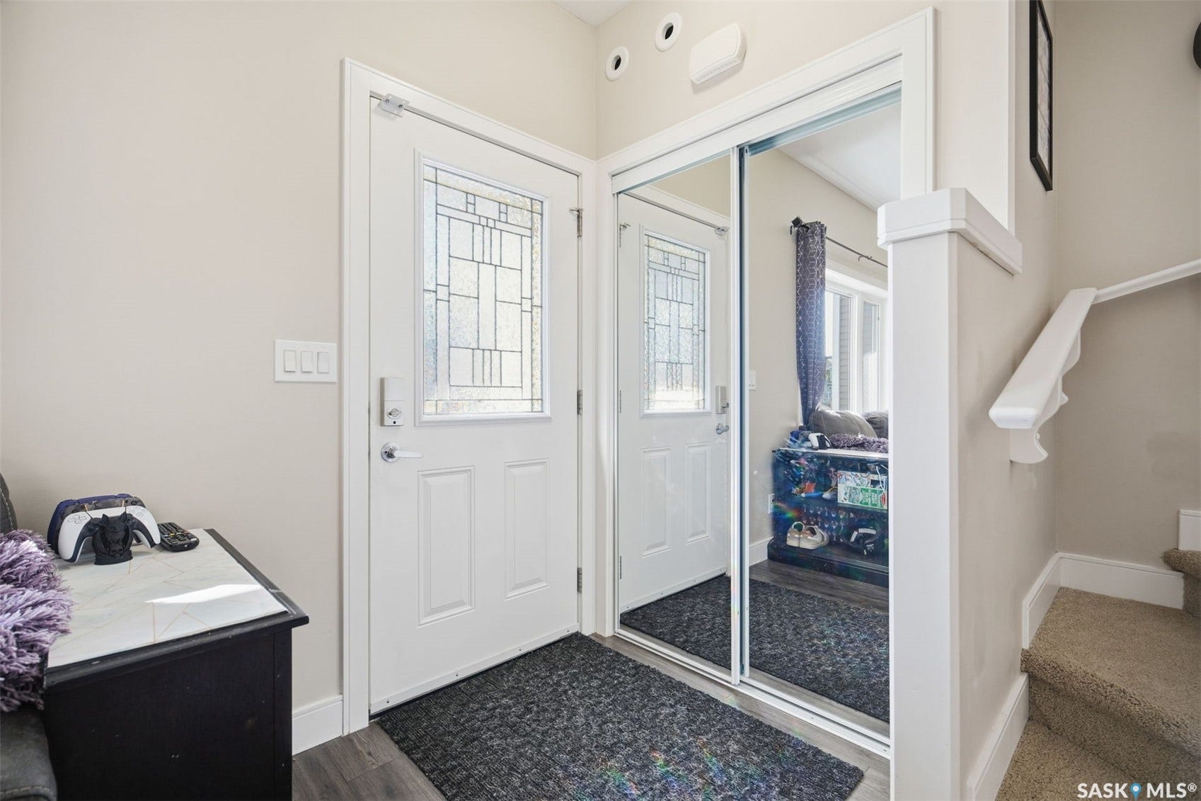 Entryway featuring a white door with decorative glass inserts, mirrored closet doors, and wood-finish flooring