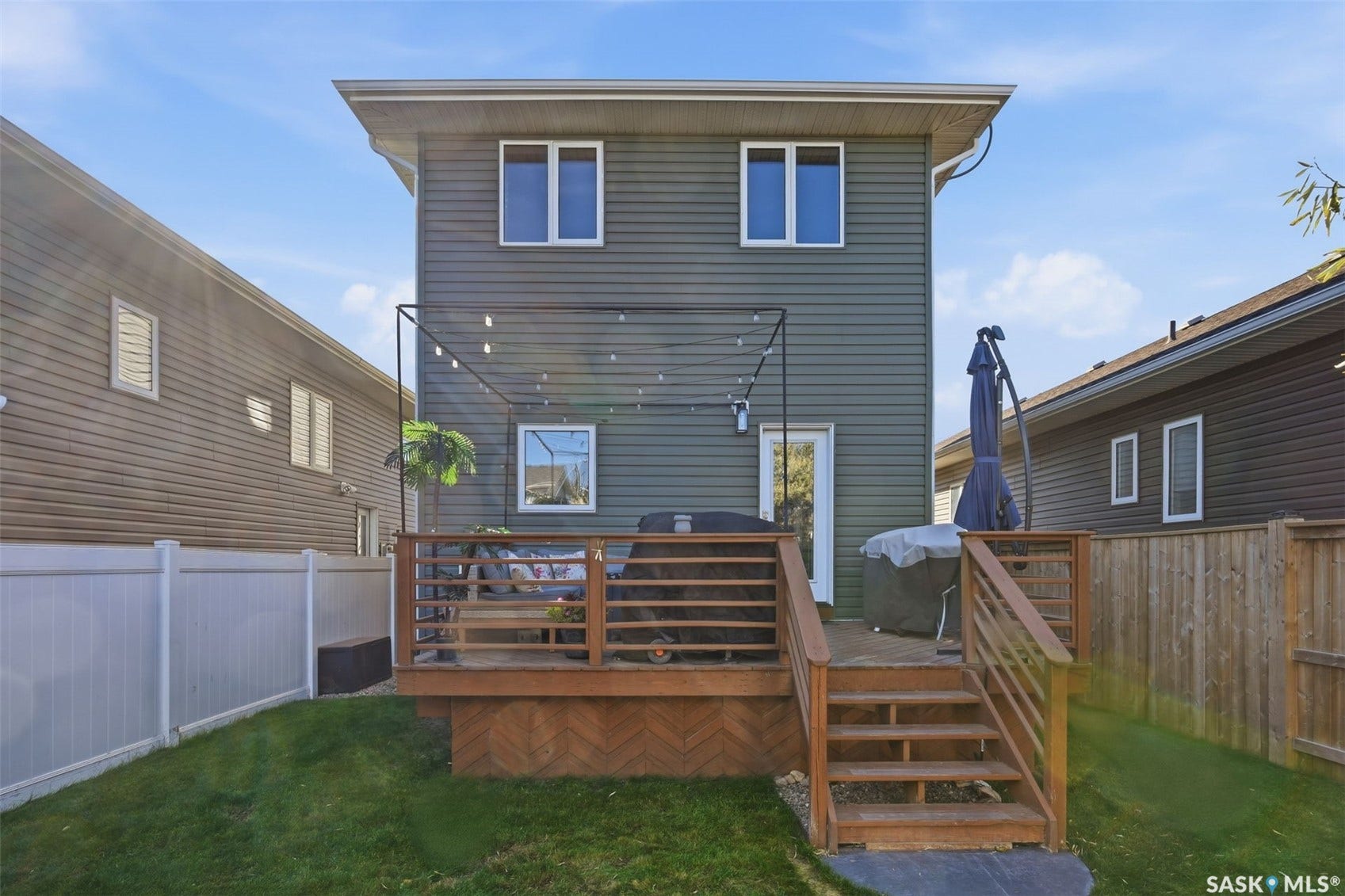Wood deck with steps to a grass yard, featuring a white privacy fence and a wooden fence