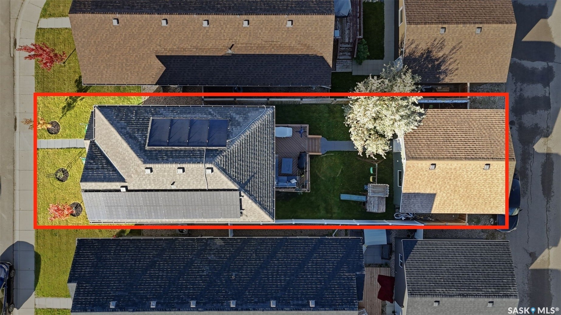 Gable roof with solar panels, attached garage, manicured lawn, and backyard deck