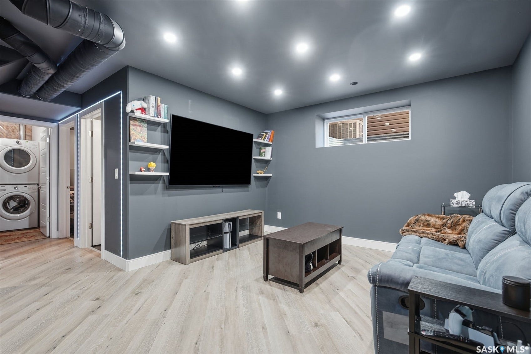 Recessed lighting, wood-finish flooring, a wall-mounted television, built-in shelving, and a stacked washer and dryer